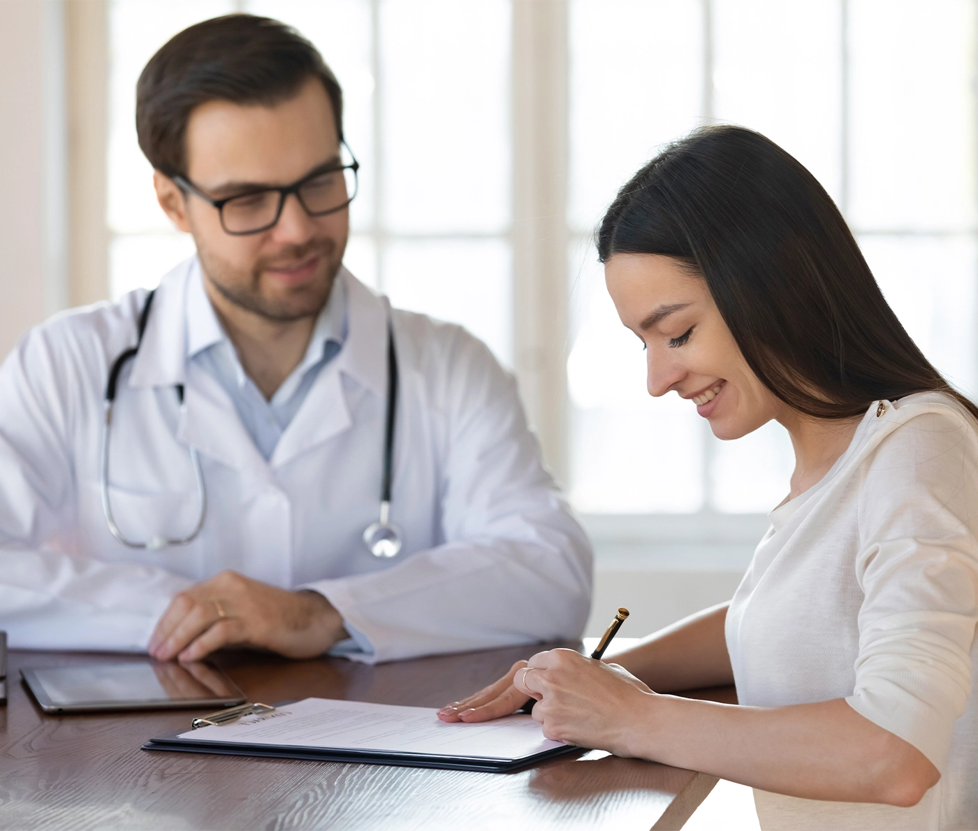 Smiling female Caucasian patient sign paper contract make health insurance agreement with male doctor in clinic. Woman client put signature on document close deal with therapist on private hospital.