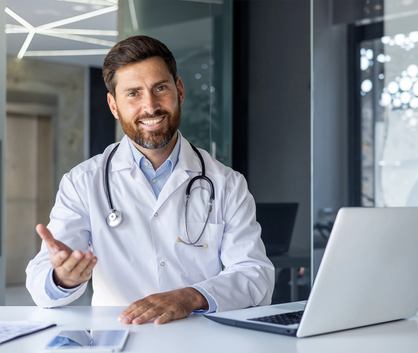 Portrait of a smiling young male doctor talking and consulting on a video call. He is sitting at the table in the office of the clinic