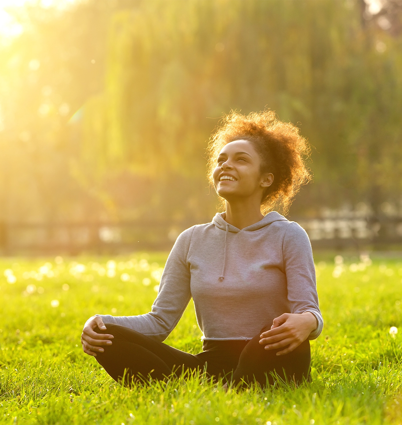 Happy young woman sitting outdoors in yoga position