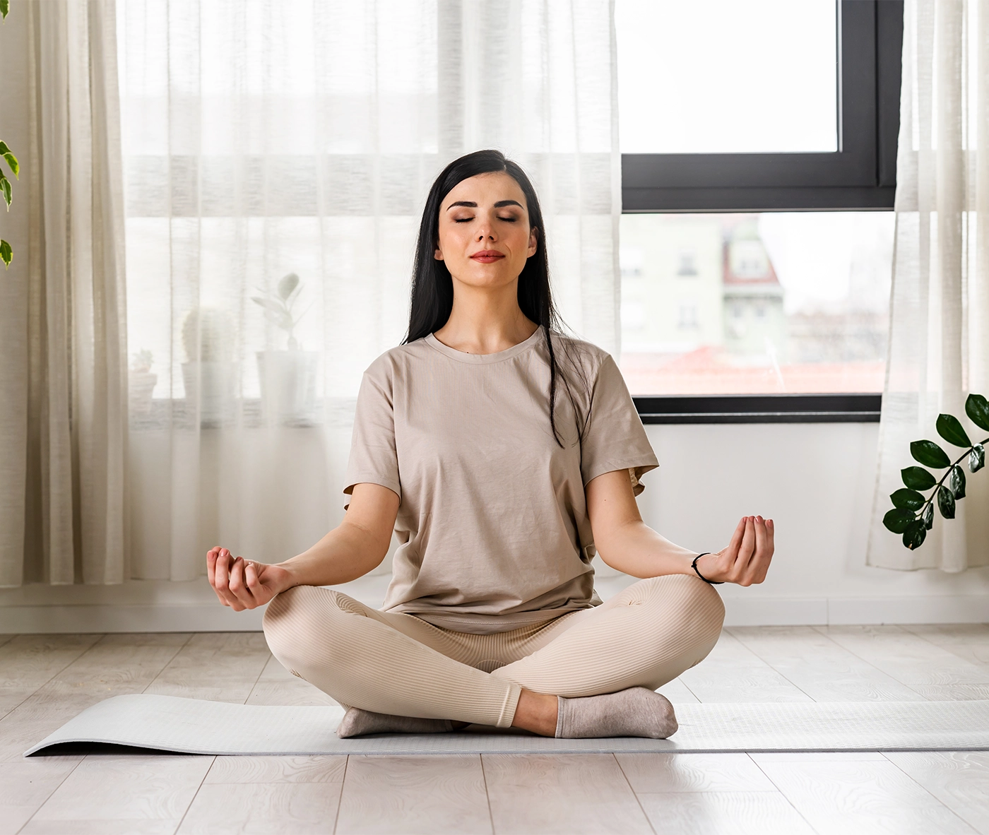 Young woman meditating sitting on a yoga mat near a big window