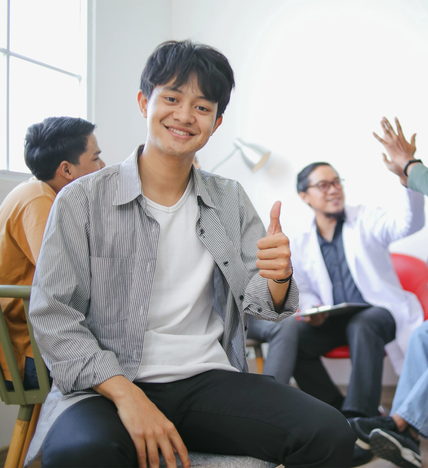 Cheerful Young Asian Man Giving Thumb Up Against Group Psychological Counseling Background
