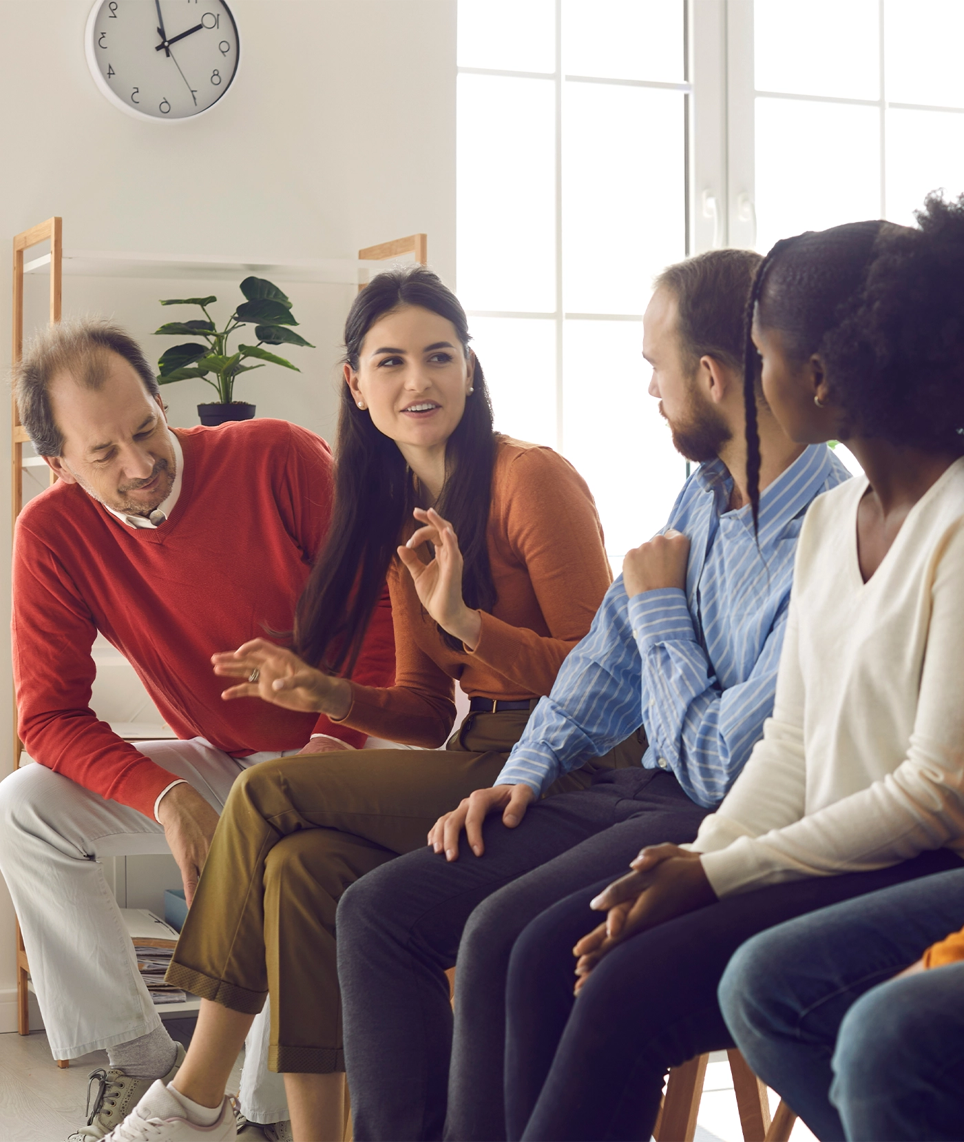 Team of diverse interested people sitting in row and listening to young woman sharing opinion in office meeting