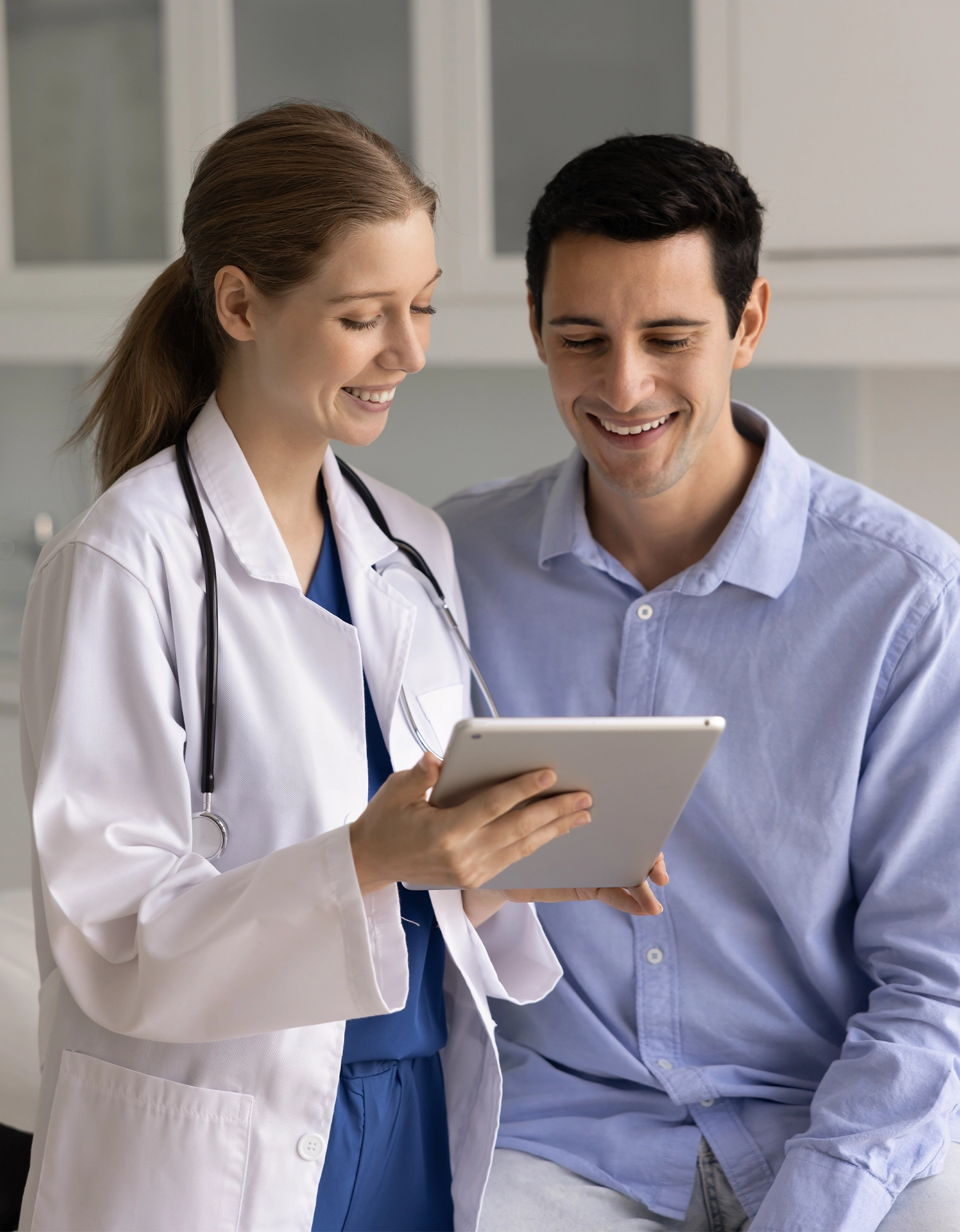 Happy physician woman explaining checkup electronic report to positive Latin male patient, showing content on tablet computer
