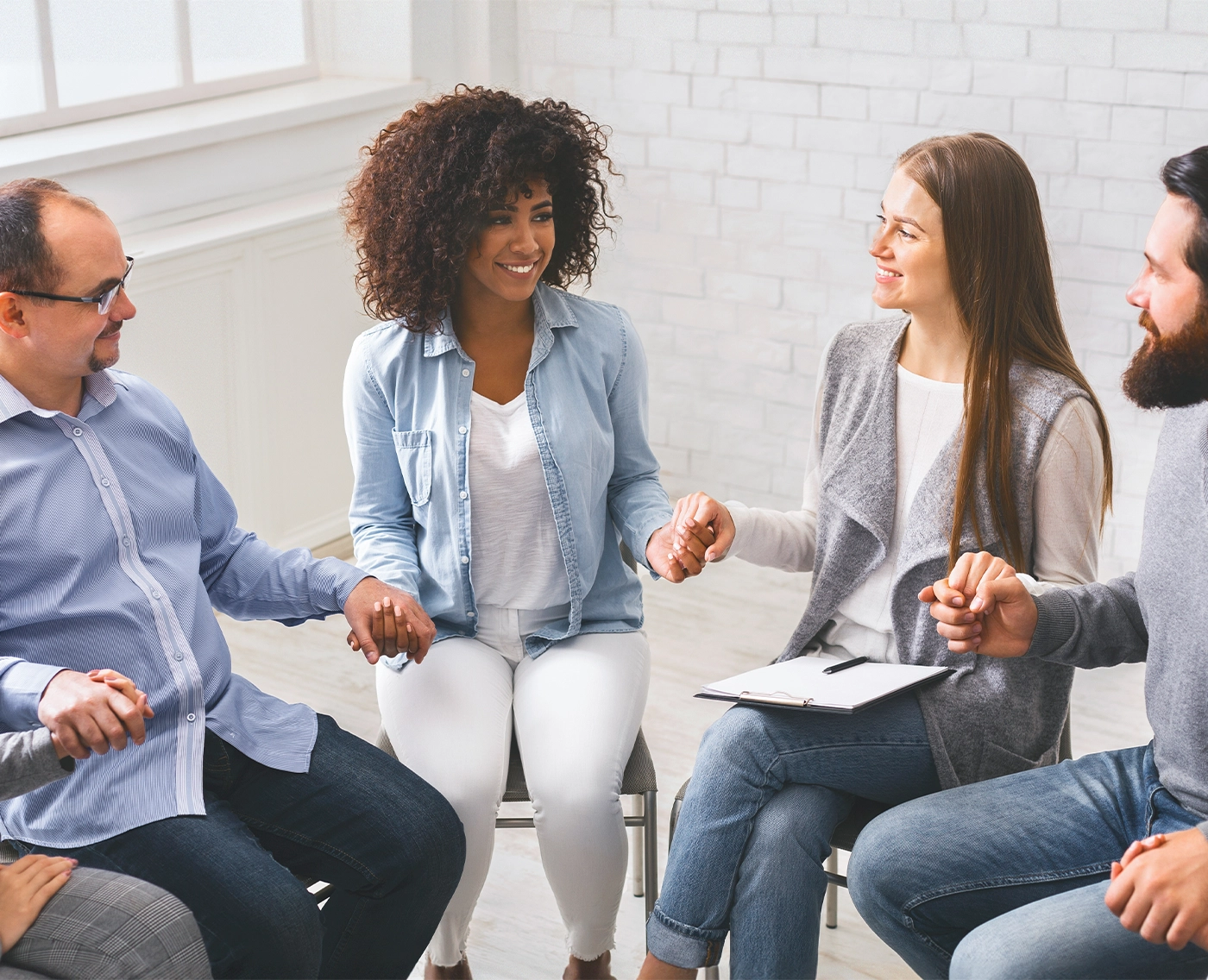 young multi-cultural group of people holding hands during therapy session, sitting in trust circle and smiling