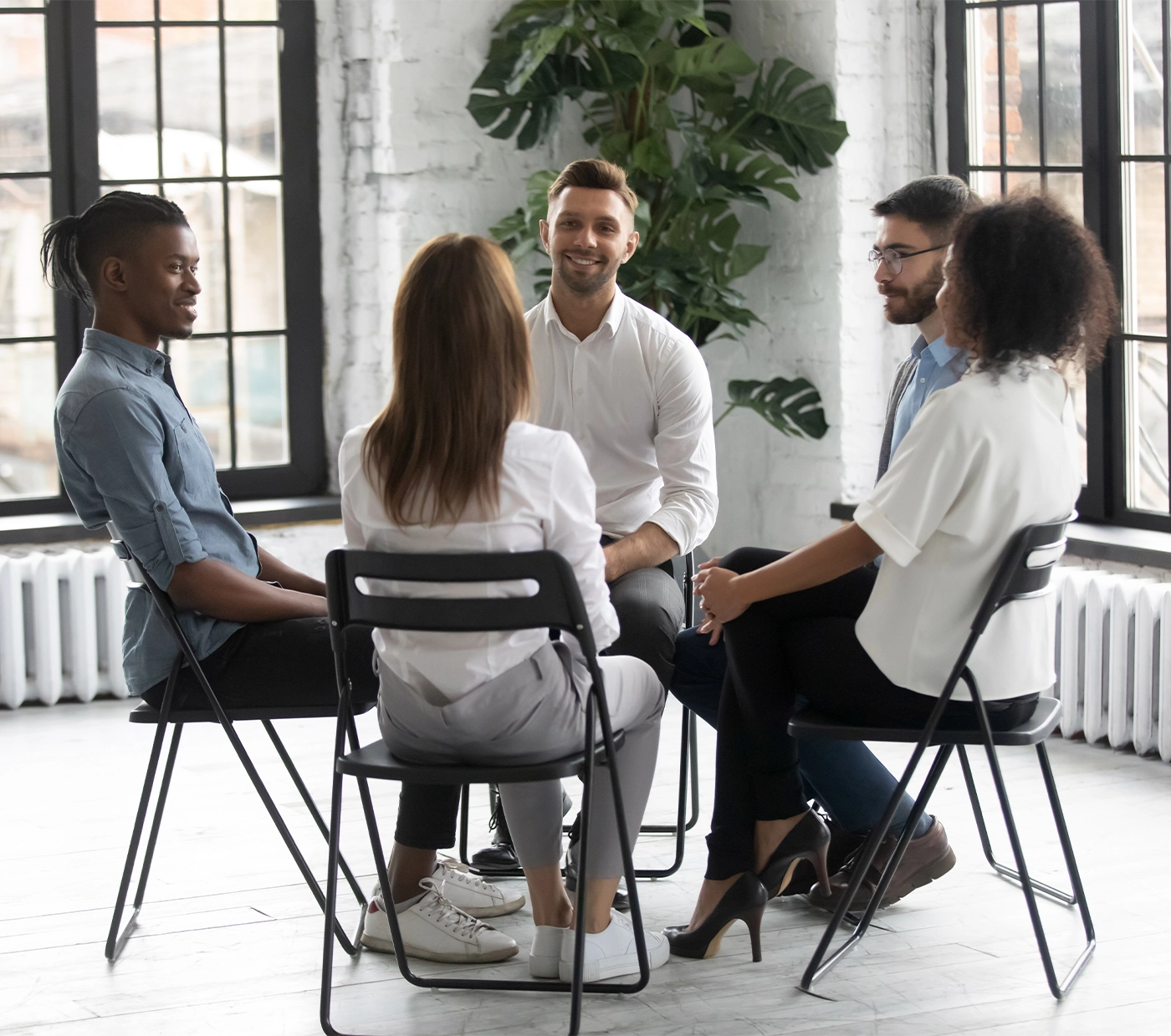 Smiling diverse multiracial colleagues sit in circle participate in motivational teambuilding or training together, multiethnic people take part in psychological session or therapy, give help support