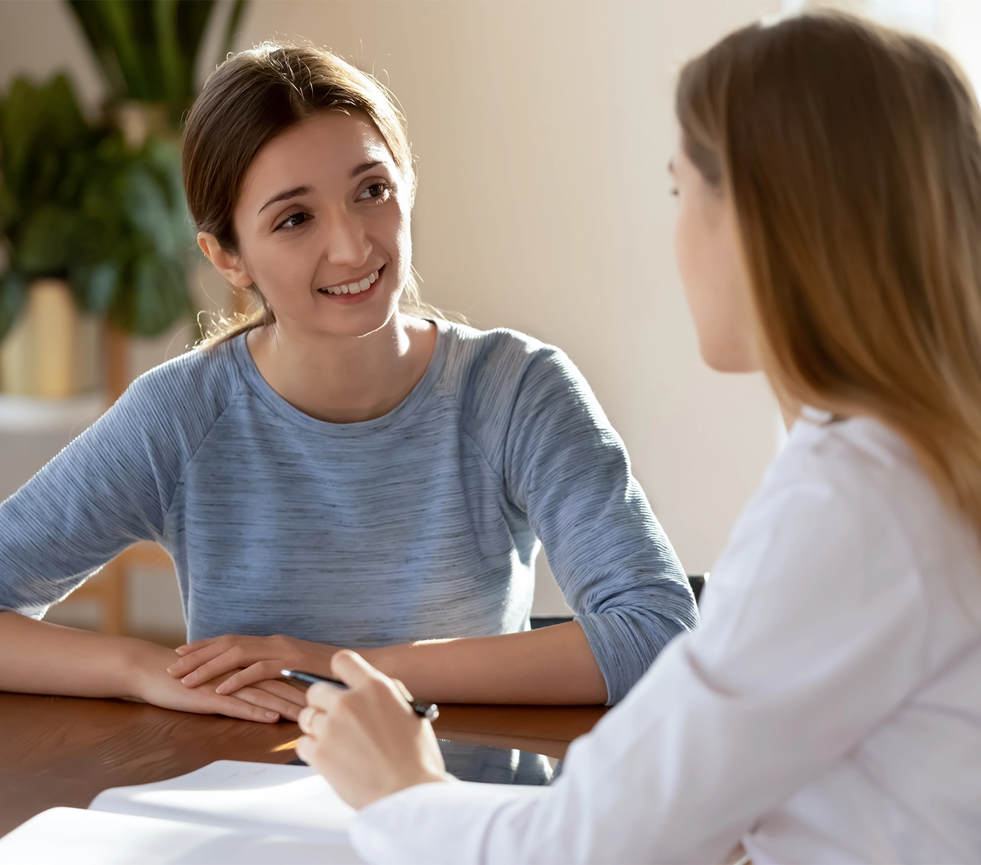 Smiling young woman listening to doctor therapist at meeting, sitting at work table in hospital, physician consulting patient about checkup results, giving recommendations at medical appointment