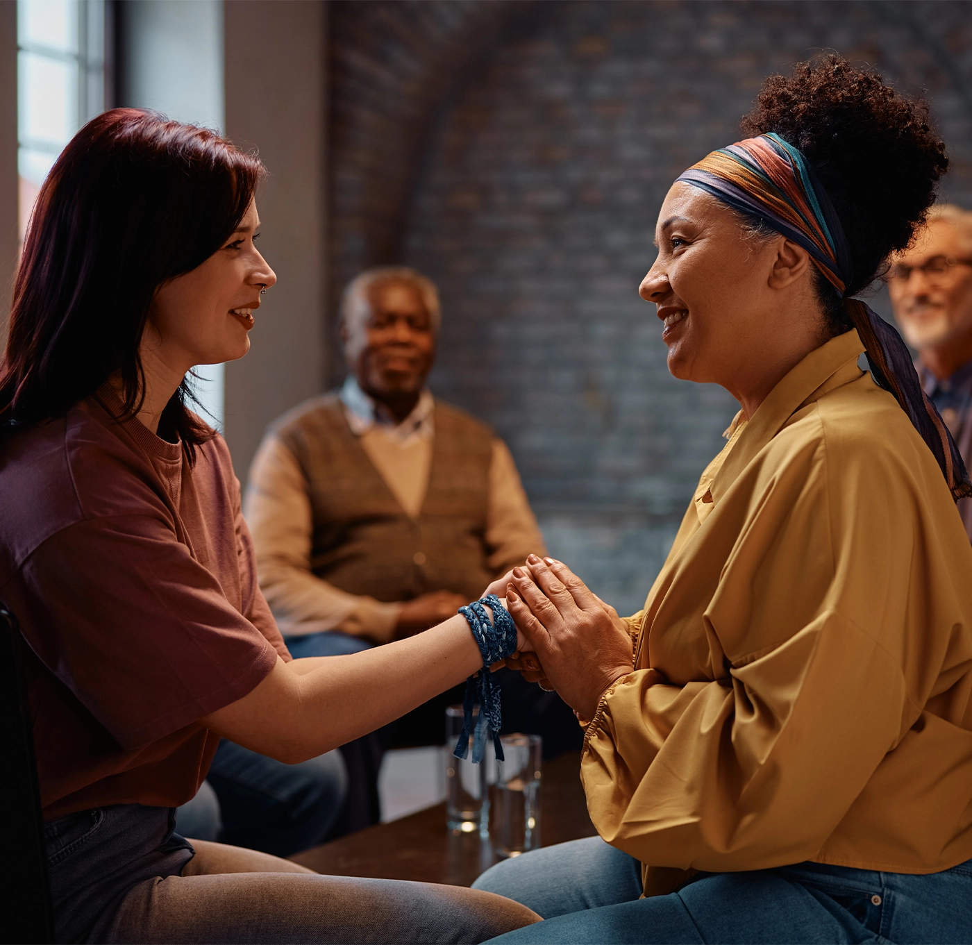 Supportive women holding hands during group therapy at mental health center.