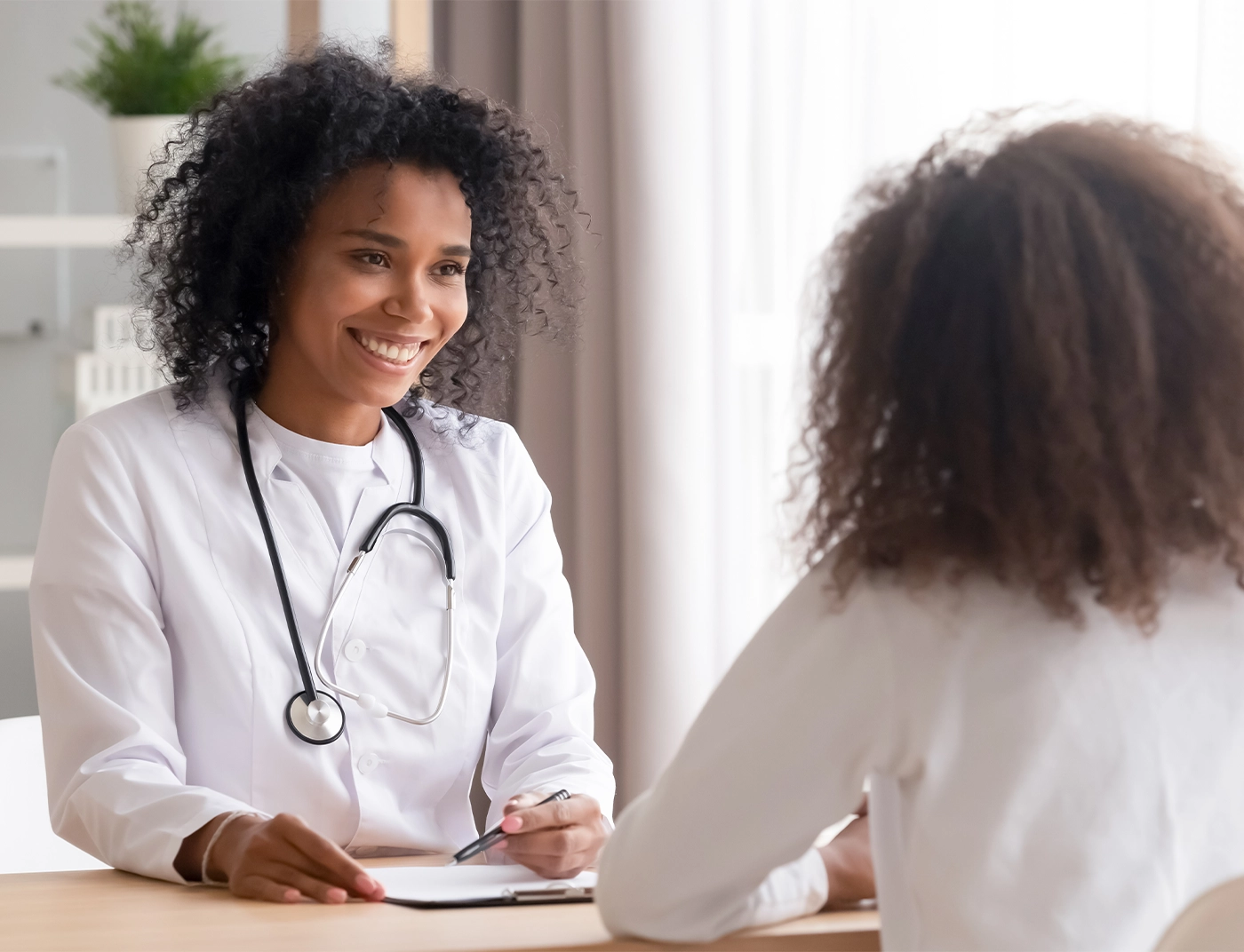 Smiling african american female doctor talking to teen patient making notes in clipboard listening to black kid school teenage girl tell complaints fill form at medical clinic checkup appointment.