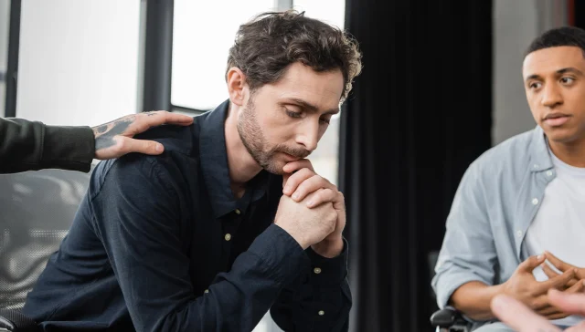 Multiethnic people calming upset person during alcoholics meeting in rehab center