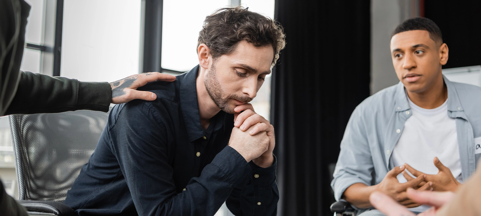 Multiethnic people calming upset person during alcoholics meeting in rehab center