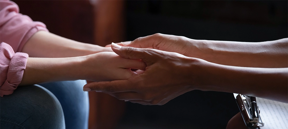 Different ethnicity female friends hold hands during confidential talk close up. Counsellor psychologist provide mental aid to patient at session in clinic, addicted patient professional help concept