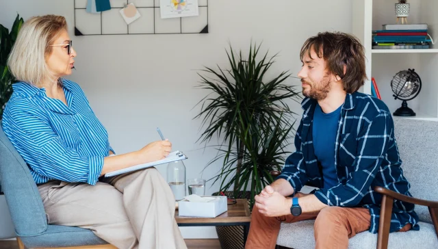 Depressed male patient having psychotherapy session with counselor at mental health clinic. Man with emotional problems consulting professional therapist i comfy office. Psychological help service.