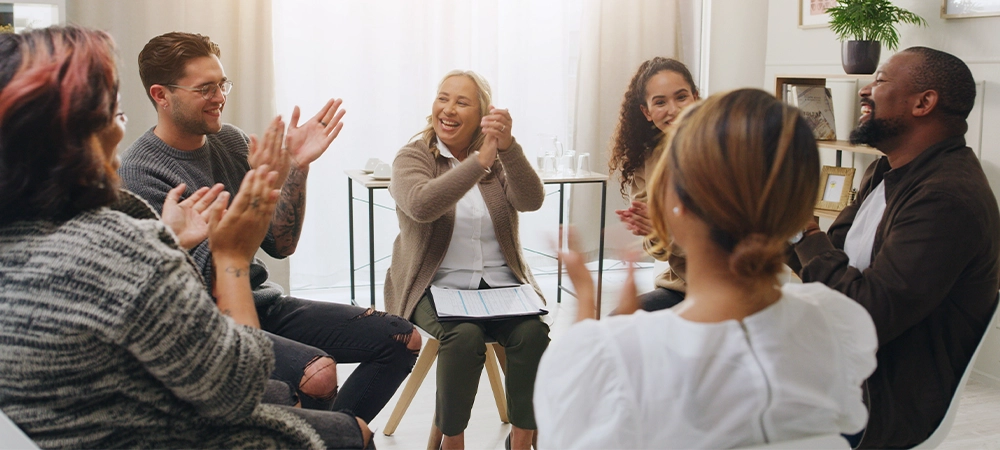 Meeting, applause and therapy with people in support group for sobriety millstone, community and success. Recovery check in, achievement and counseling workshop with men and women for celebration