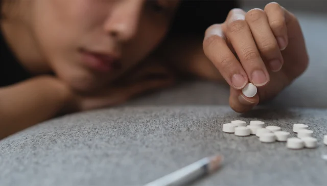 drug addict asian young woman hand holding pills, medicament with narcotic syringe on sofa at home, abuse overdose