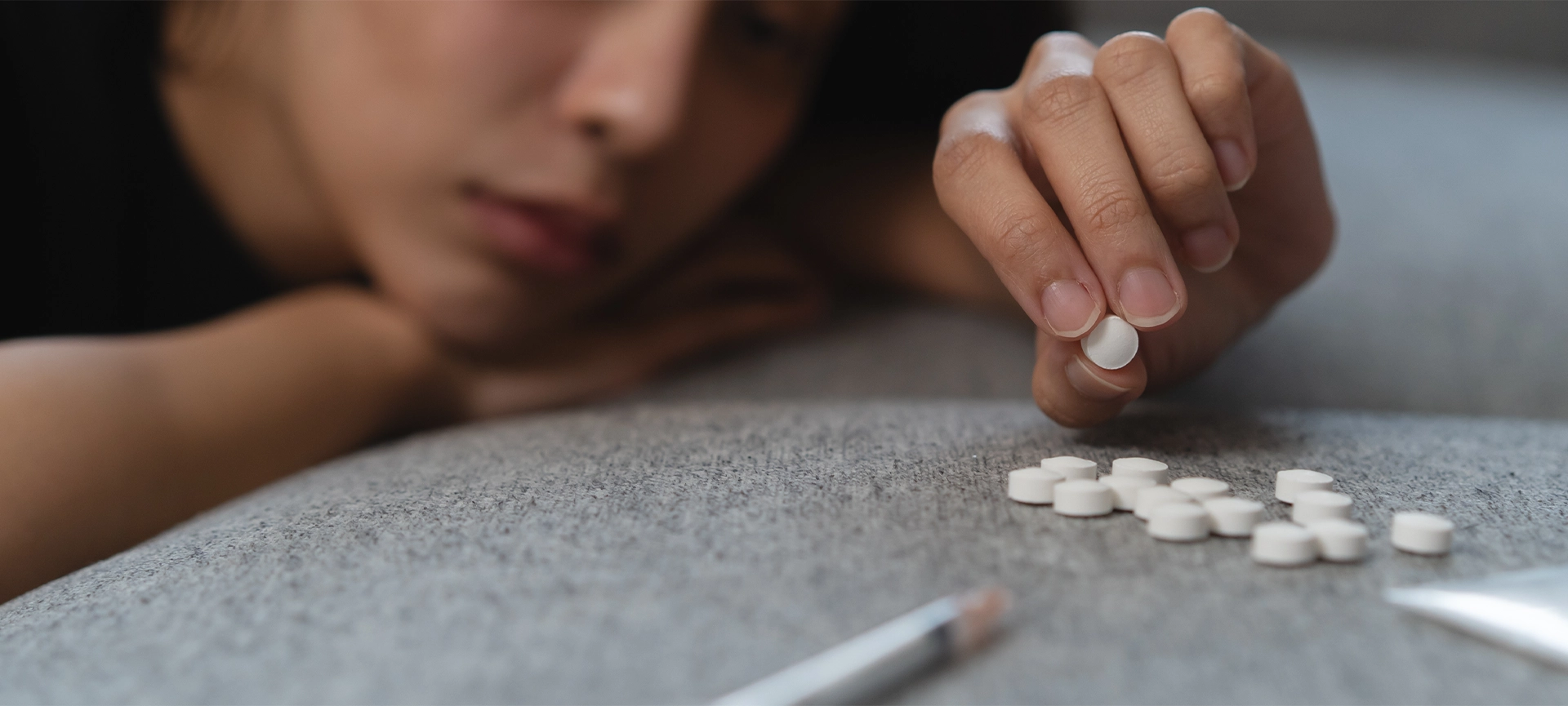 drug addict asian young woman hand holding pills, medicament with narcotic syringe on sofa at home, abuse overdose
