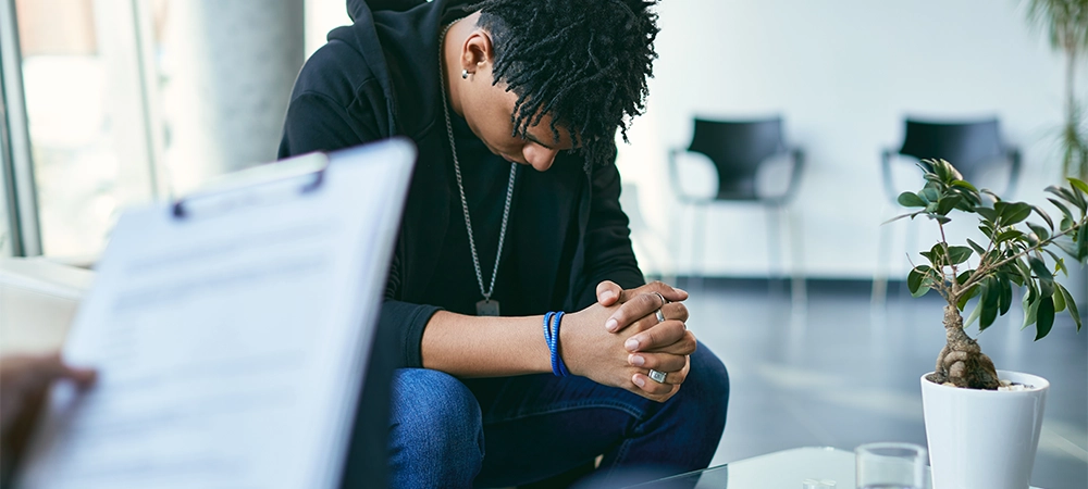 Depressed black teenage boy having counselling with mental health professional.