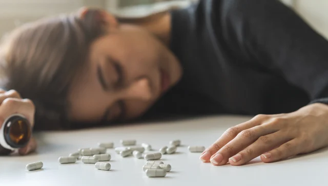 Anti drugs, drug addict, asian young woman, girl hand holding pills bottle, unconscious on table at home, abuse overdose. Sick pain of health, unhealthy people. Suicide depressed or despair.
