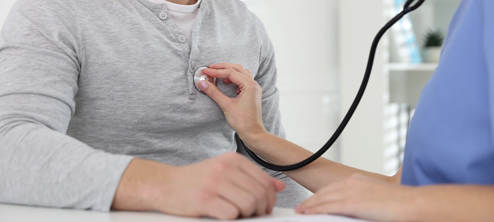 Doctor checking man's heartbeat with stethoscope in hospital, closeup