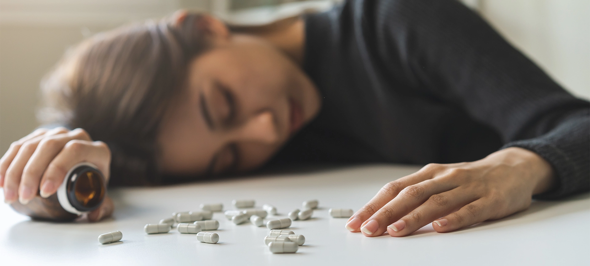 Anti drugs, drug addict, asian young woman, girl hand holding pills bottle, unconscious on table at home, abuse overdose. Sick pain of health, unhealthy people. Suicide depressed or despair.