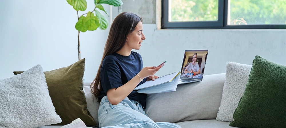 Teenage girl having online therapy sitting at home using laptop for video meeting with counselor