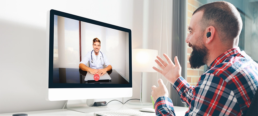 Young man sitting in front of the computer talking to his doctor through a video conference. Online medicine concept