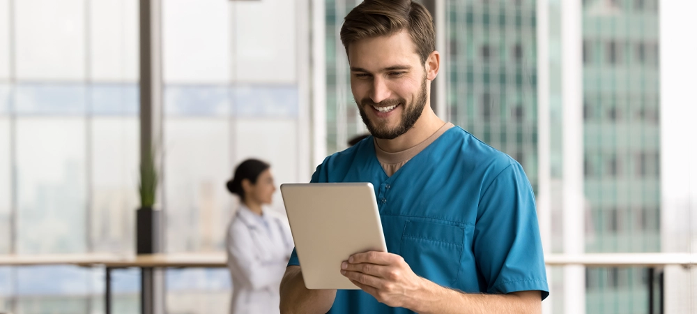 Young man medical worker wear blue scrubs using tablet in clinic, leading telemedicine consultations, conducting virtual meetings with patients, prescribing medications remotely, managing appointments