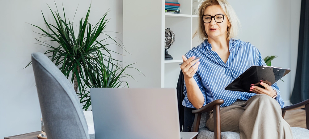 Professional Psychotherapy online. Middle aged female Psychologist having video call consultation on laptop while sitting on armchair In office. Specialist talking, counseling, helping patient online