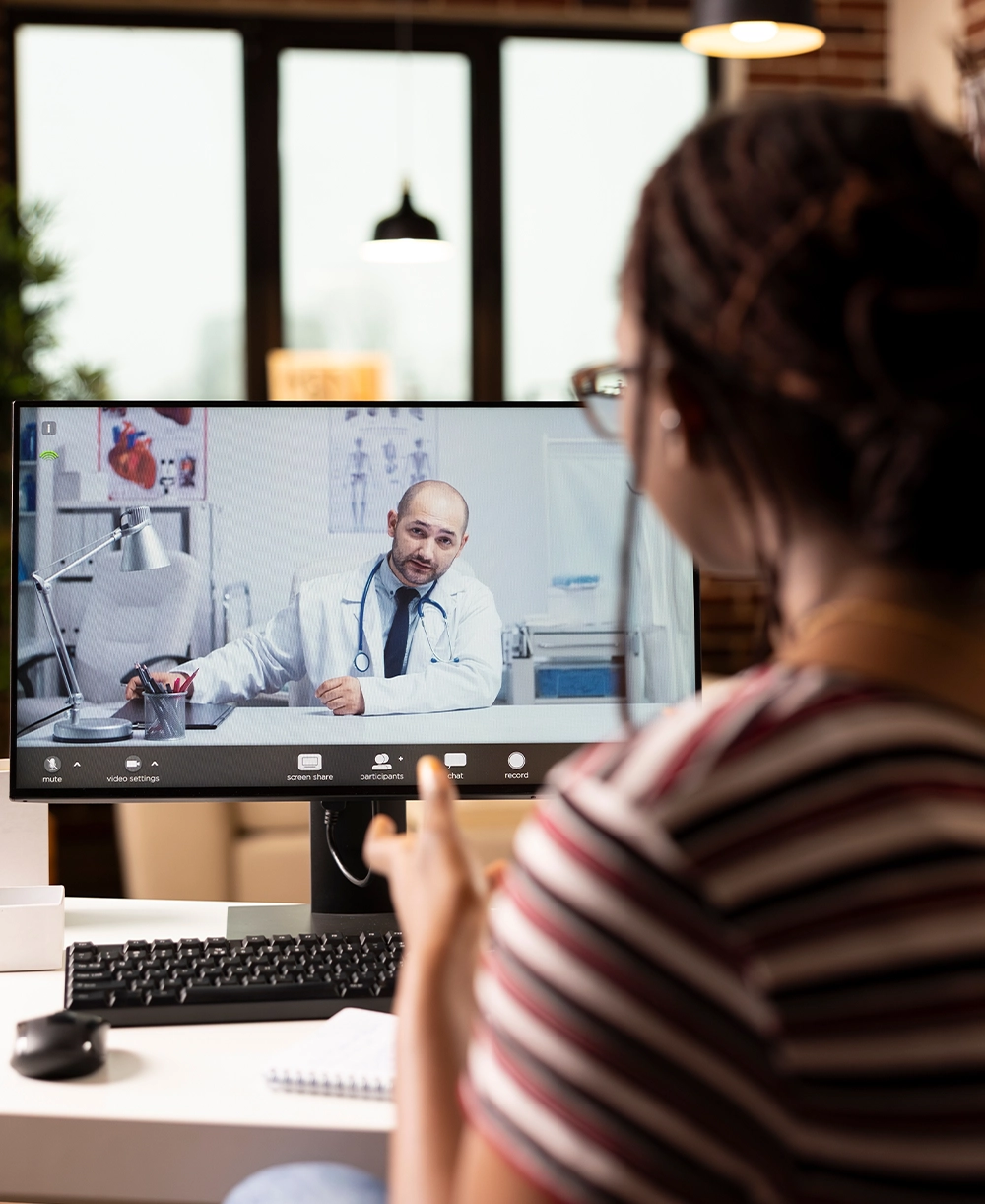 Close up of female patient attending virtual medical consultation at home. Computer screen shows caucasian male doctor speaking with black woman during online healthcare appointment.
